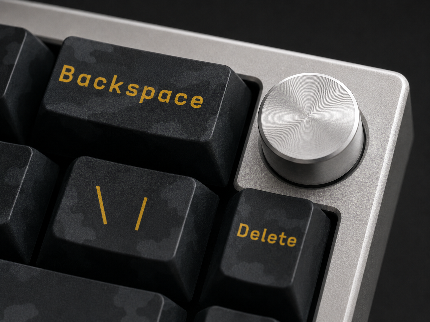 Close-up of the C01's corner: the machined aluminum rotary knob, the Backspace and Delete keycaps, and the bead-blasted case edge